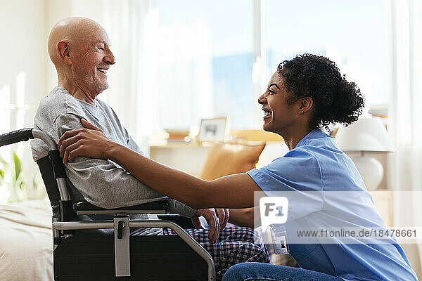 Happy physiotherapist talking to senior man sitting on wheelchair