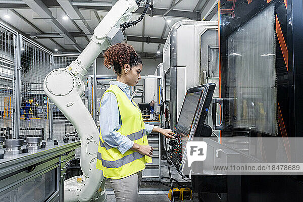 Engineer standing by robotic arm and operating machine in factory