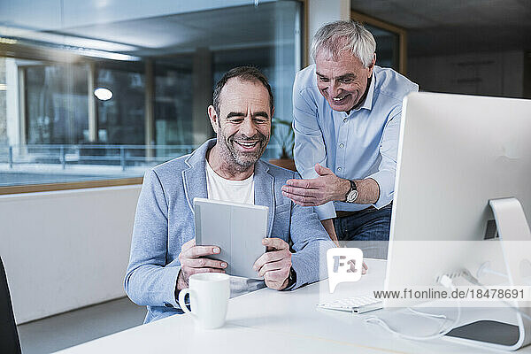 Zufriedene Geschäftskollegen teilen sich einen Tablet-PC im Büro