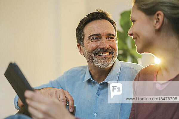 Smiling mature man talking to woman with tablet PC at home