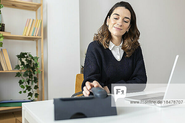 Smiling businesswoman holding telephone receiver at desk