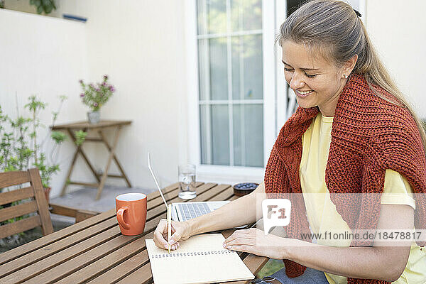 Smiling freelancer making notes on table in garden