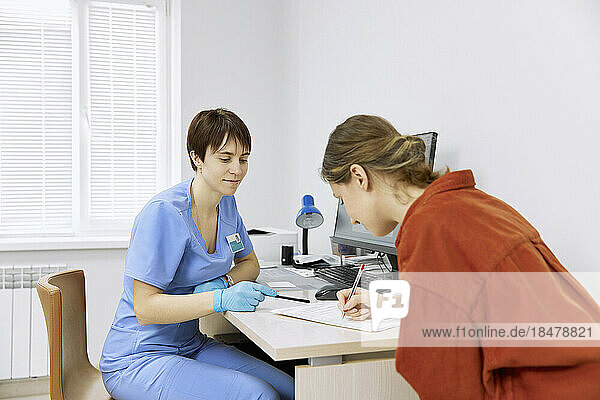 Ophthalmologist assisting patient filling form at clinic