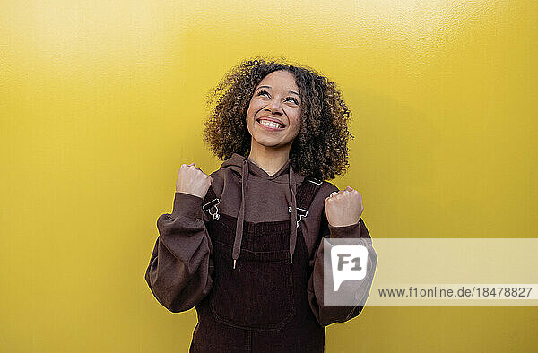 Happy woman clenching fists in front of yellow background