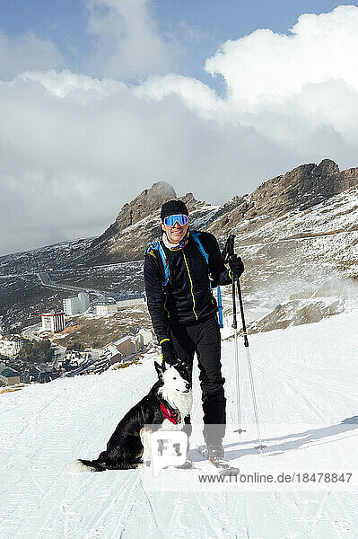Mann steht mit Skistöcken und Hund im Schnee