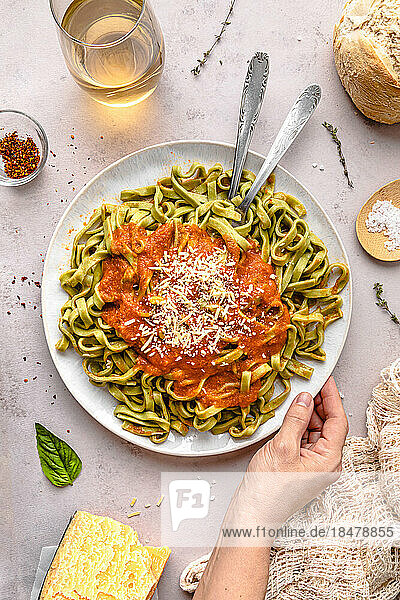 Hand of mature woman with spinach tagliatelle and tomato sauce served in plate on table