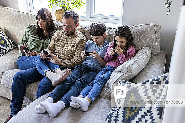 Familie benutzt Mobiltelefone auf dem Sofa im Wohnzimmer zu Hause