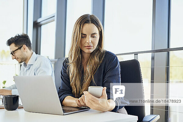 Businesswoman using smart phone by laptop at workplace