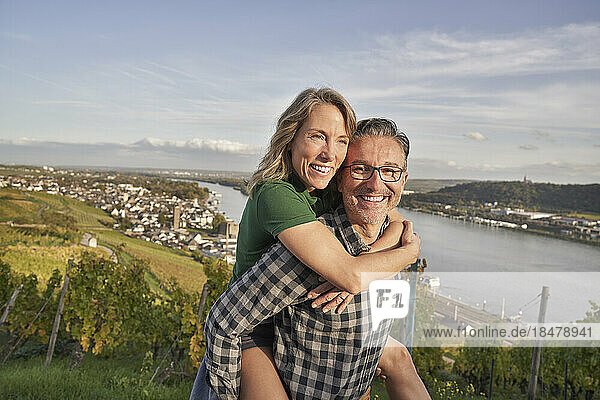 Happy man piggybacking woman by river on hill