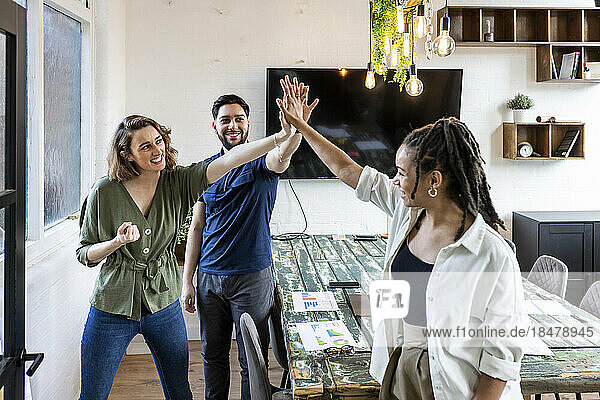 Happy businesswoman with colleagues doing high five in office