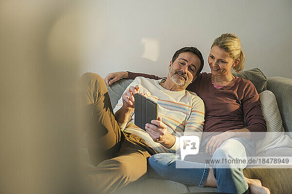 Couple sharing tablet PC sitting on sofa at home