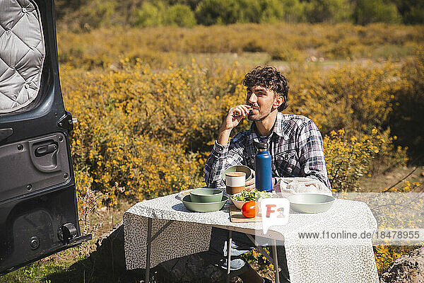 Man eating food sitting at camping table on sunny day