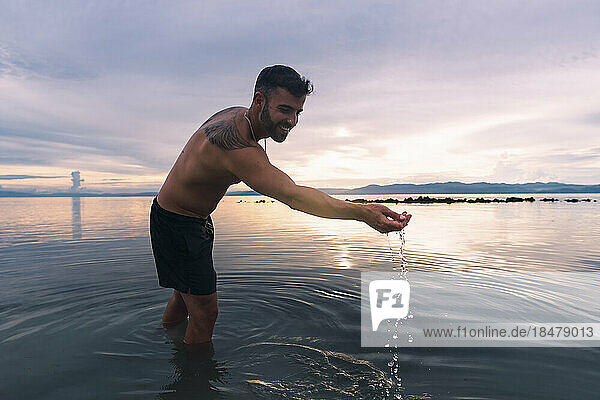 Happy man playing with water and enjoying sunset at beach