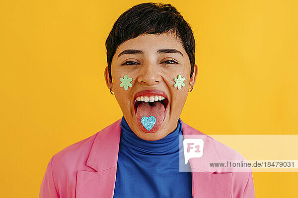 Woman with stickers on face and tongue against yellow background