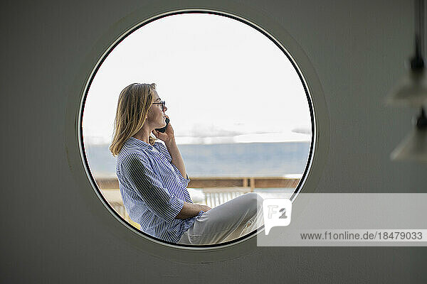 Geschäftsfrau spricht mit Smartphone und sieht durch ein kreisförmiges Fenster