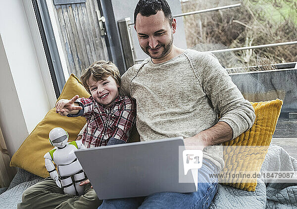 Glücklicher Sohn zeigt Friedenszeichen  während Vater zu Hause Laptop benutzt