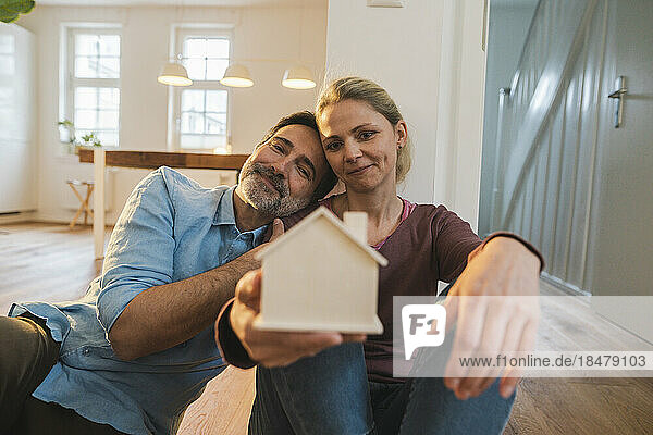 Smiling couple looking at house model sitting at home