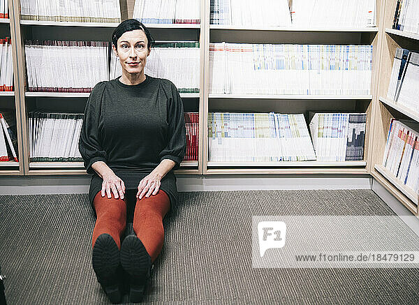 Smiling woman sitting in front of bookshelf in library