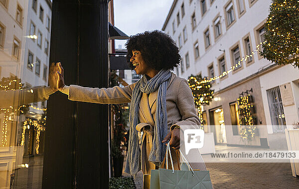 Happy young woman touching glass of store window at footpath