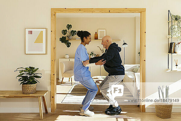Home caregiver assisting senior man in exercising at home