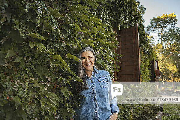 Smiling mature woman standing at overgrown facade