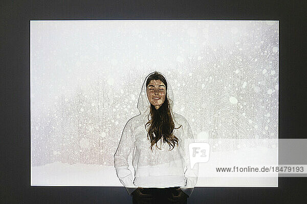 Happy woman with eyes closed standing in front of snowfall on projection screen