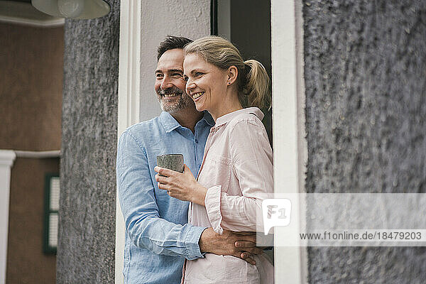 Glücklicher Mann umarmt seine Frau und hält eine Tasse vor der Tür