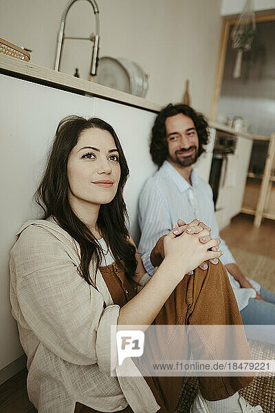 Thoughtful woman sitting with boyfriend in kitchen at home