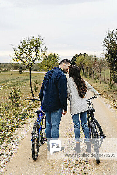 Junges Paar mit Fahrrädern küsst sich auf unbefestigter Straße