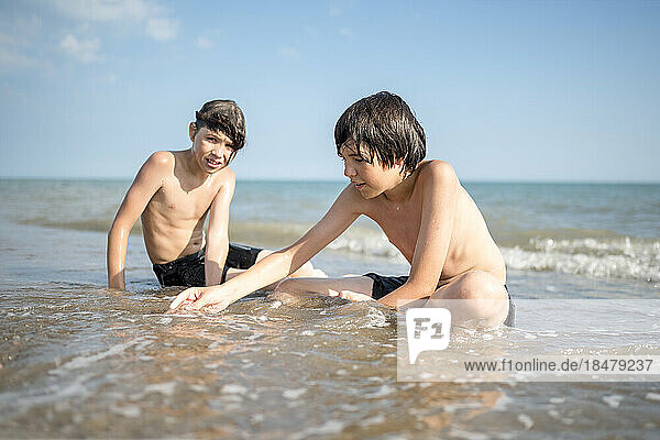Brothers playing together sitting in wet sand on shore at beach