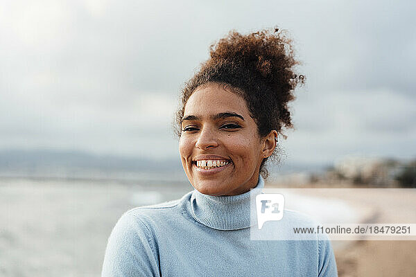 Glückliche junge Frau mit Afro-Frisur am Strand