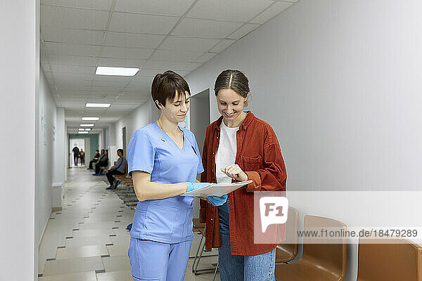 Doctor and patient reviewing test results standing in corridor at hospital