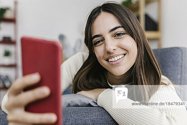 Smiling woman with smart phone lying on sofa at home