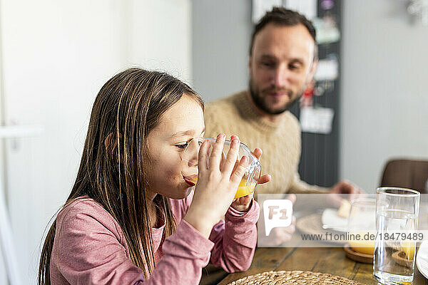 Mädchen trinkt Saft mit Vater beim Frühstück zu Hause