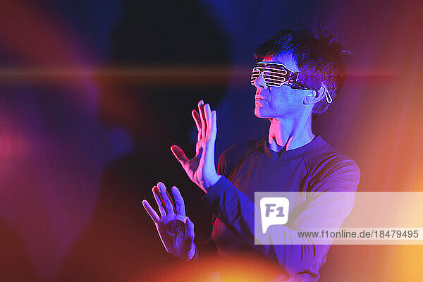 Mature woman wearing smart glasses gesturing under neon lighting