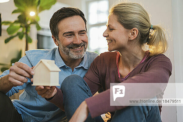 Happy couple talking to each other holding house model at home