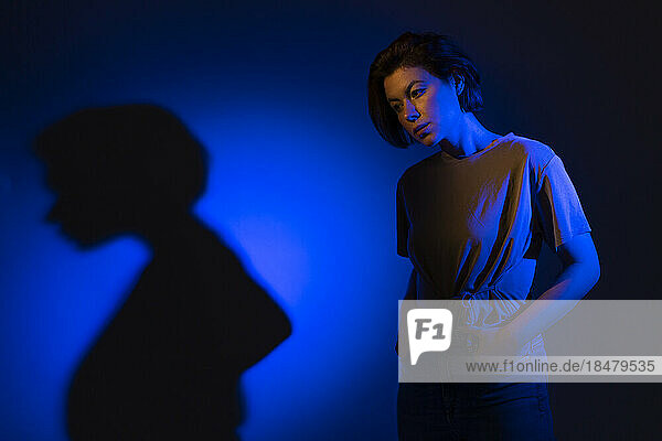 Thoughtful young woman with blue neon lighting against colored background