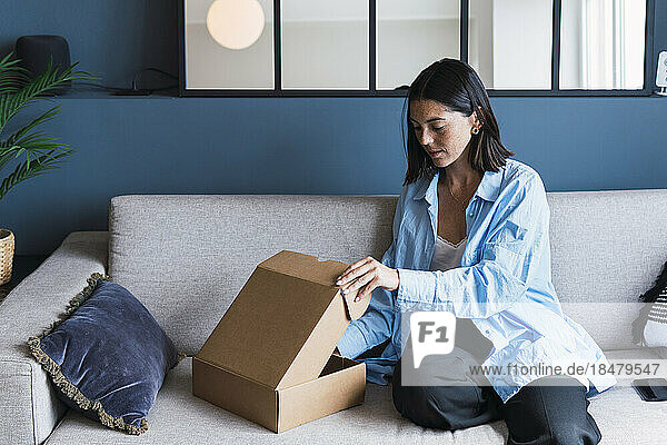 Young woman opening package on sofa at home