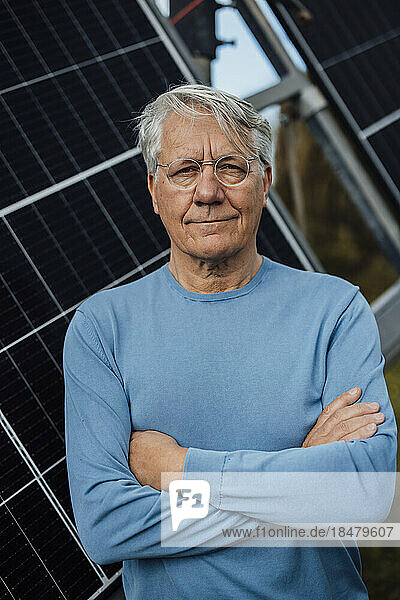 Smiling man standing with arms crossed in front of solar panels