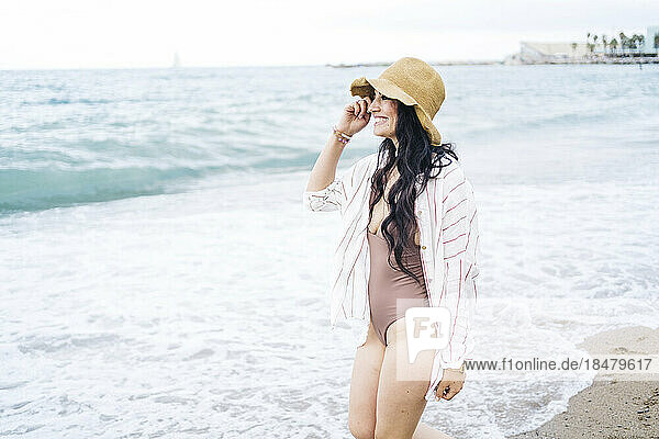 Thoughtful woman wearing hat enjoying at beach