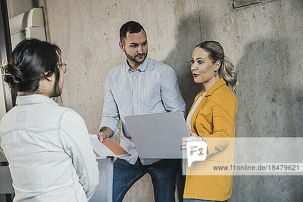 Businesswoman planning with colleagues standing near wall at office