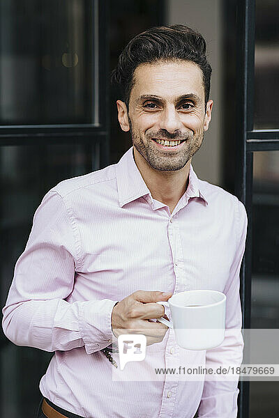 Happy mature businessman holding coffee cup at door