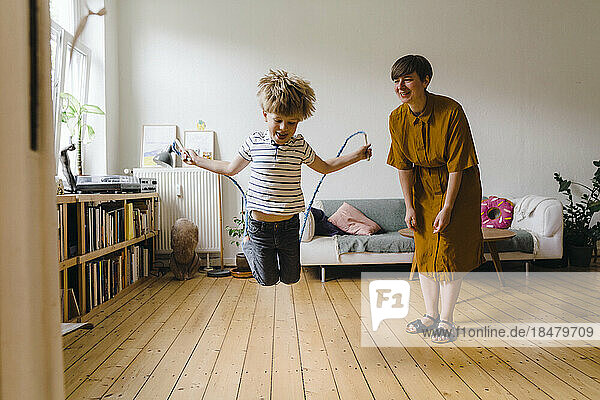 Mother cheering son playing with jump rope in living room at home