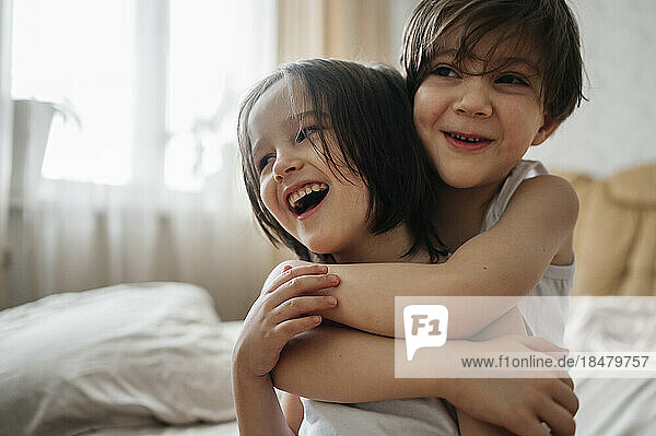 Happy boy hugging brother in bedroom at home