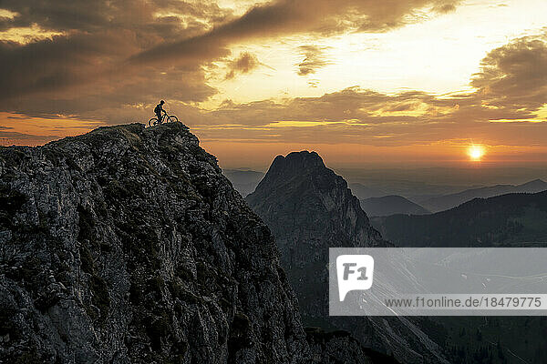 Mann mit Fahrrad auf dem Gipfel des Berges bei Sonnenuntergang