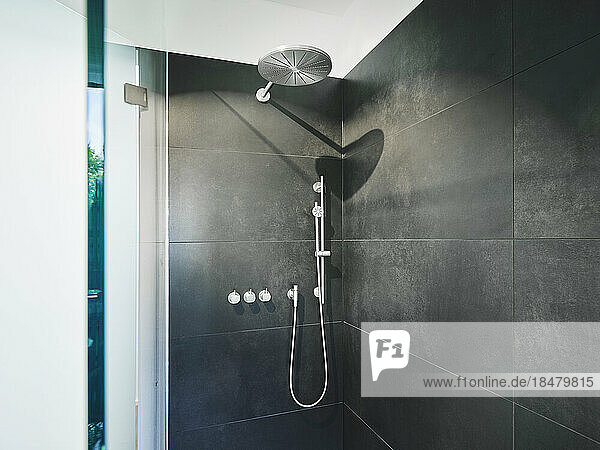 Shower amidst black tile wall in bathroom of modern apartment