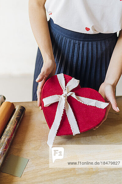 Frau steht mit herzförmiger Geschenkbox am Schreibtisch
