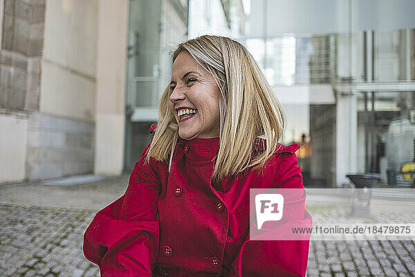 Reife Frau im roten Mantel lacht vor dem Gebäude
