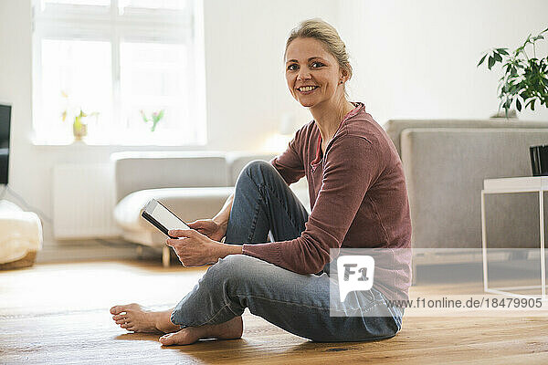 Happy woman with tablet PC sitting on floor at home