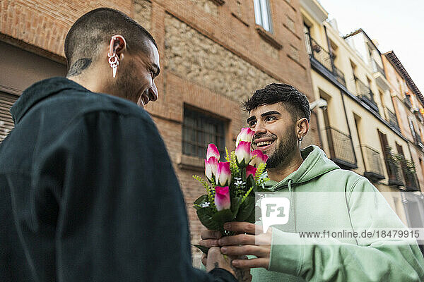 Smiling gay man giving flowers to boyfriend outside building